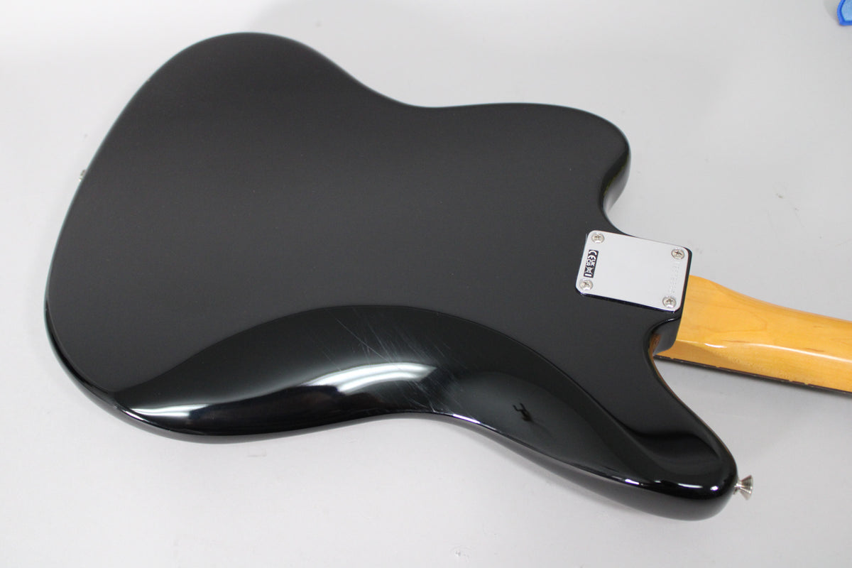 The black guitar's back is angled, showing a glossy finish with light scratches, a chrome neck plate, and a blonde maple neck.