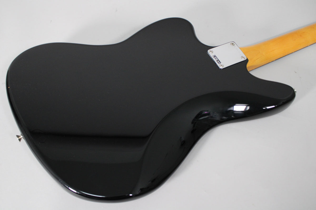 The back of a glossy black Jaguar guitar, angled from the lower left, with a light wood neck and chrome neck plate visible.
