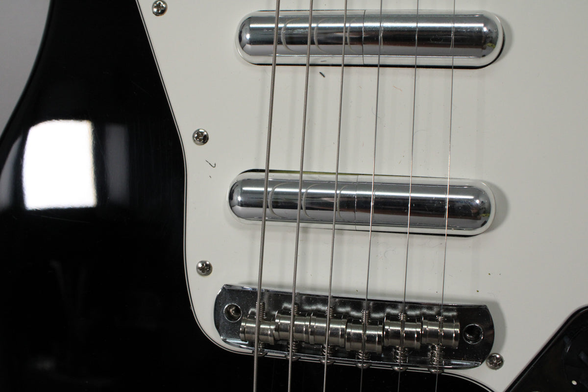 Close-up of the black guitar body and white pickguard, showing two chrome pickups, a chrome bridge, and six strings.