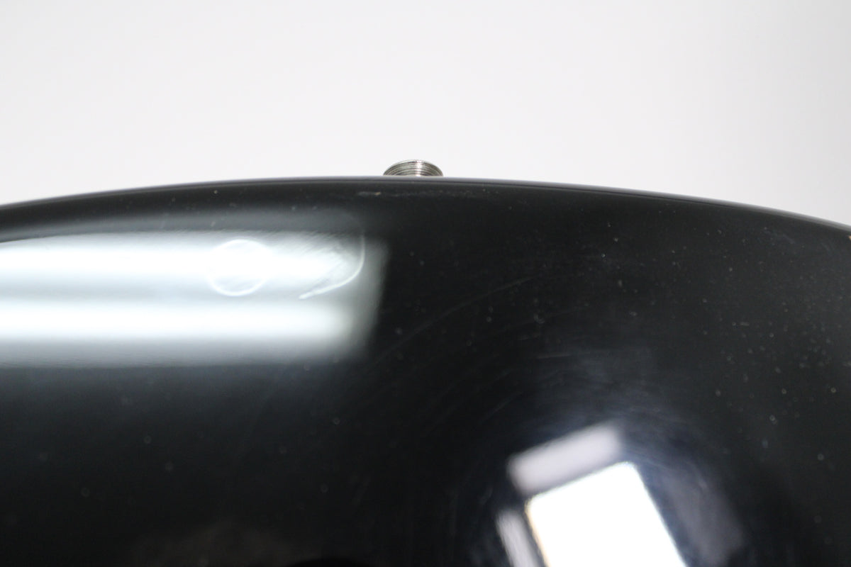 Close-up of the guitar's glossy black body, showing light scratches and a chrome strap button at the top edge.