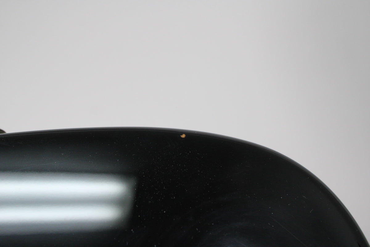 Close-up of the upper curve of the black guitar body, showing a small, light brown chip in the finish near the top edge.