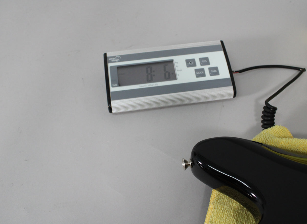 The guitar's black body, resting on a yellow cloth, is partially visible next to a digital scale displaying "8.6".