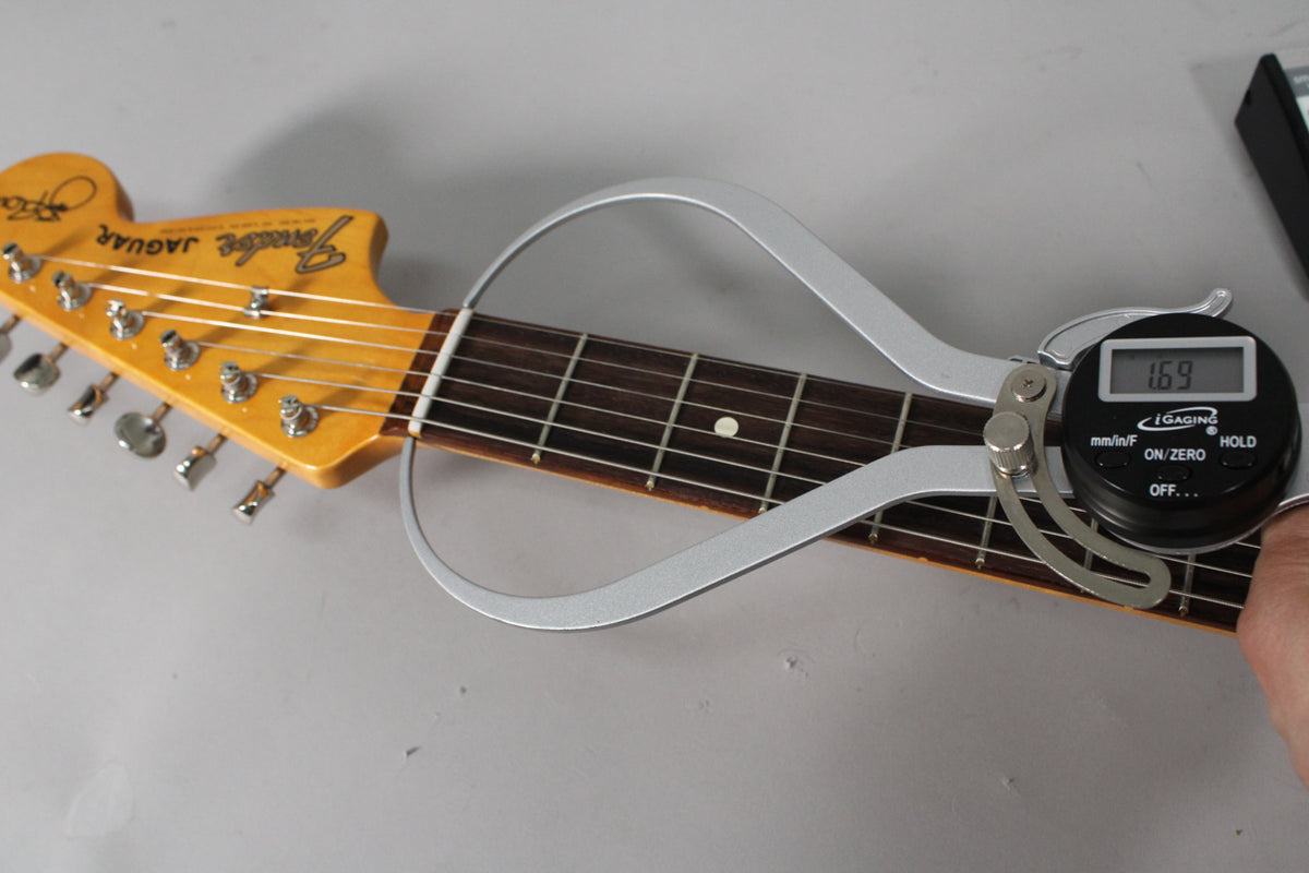 Close-up of the guitar's headstock and fretboard, with a digital caliper measuring the nut width at 1.69 inches.