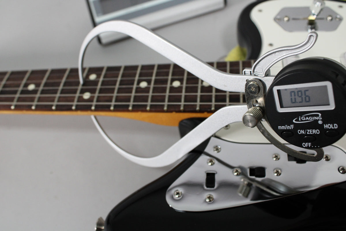 A digital caliper measures the fret height on the dark rosewood fretboard of the black guitar, showing 0.96mm.