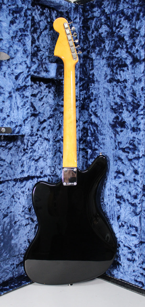 The black Jaguar guitar is shown from the back, with a glossy finish, light maple neck, and chrome tuners, resting in a blue velvet case.
