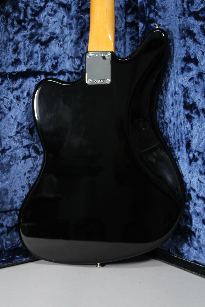 The back of a glossy black electric guitar body, with a light wood neck and chrome neck plate, resting in a blue velvet case.