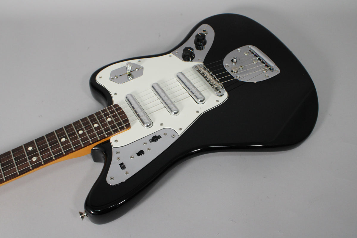 Black Jaguar electric guitar, angled top-down, showing the glossy body, white pickguard, chrome hardware, and dark fretboard.