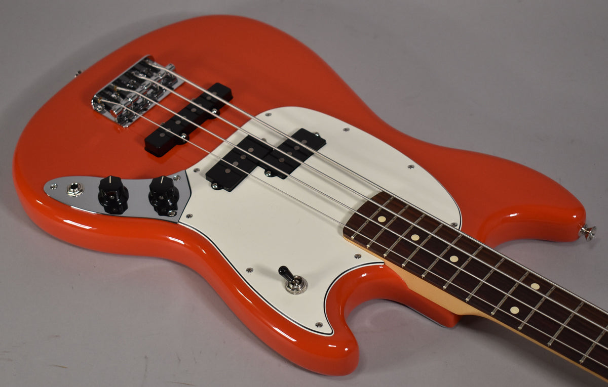 The Rallye Orange bass, angled from the lower bout, shows its white pickguard, chrome bridge, and two black control knobs.