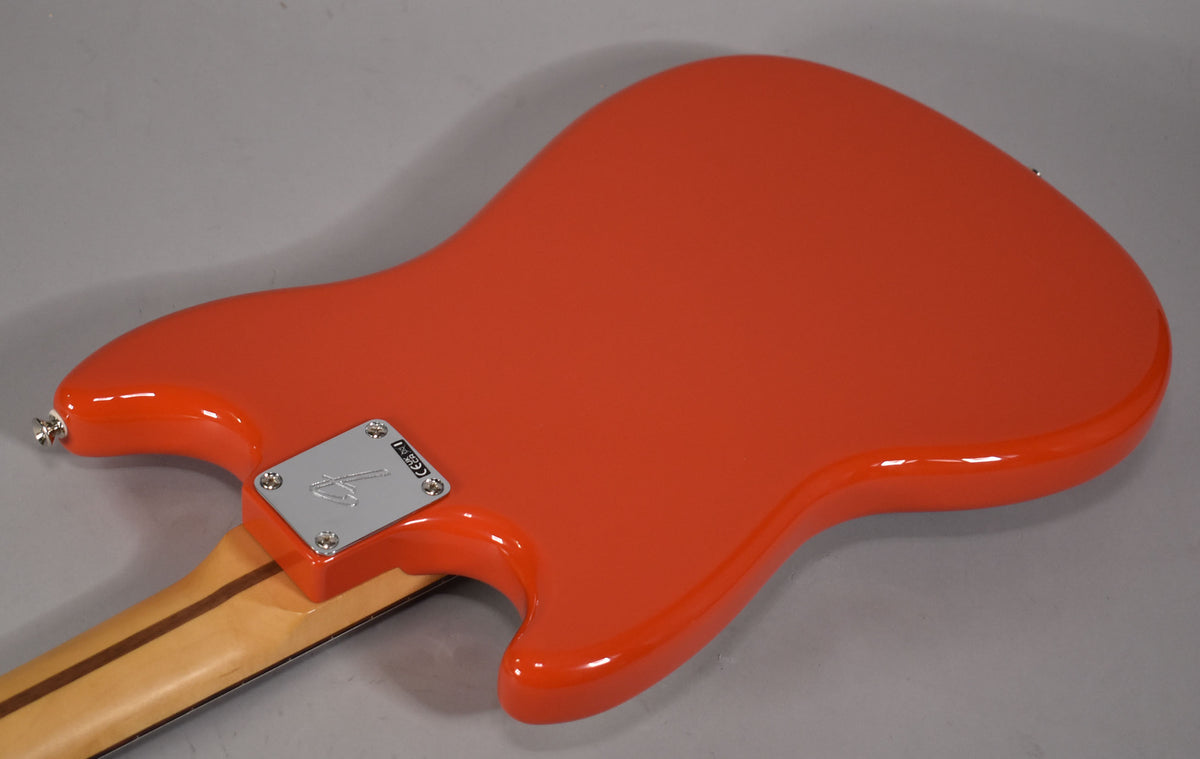 The back of a glossy orange bass guitar, angled from the lower left, showing the neck plate and strap button.