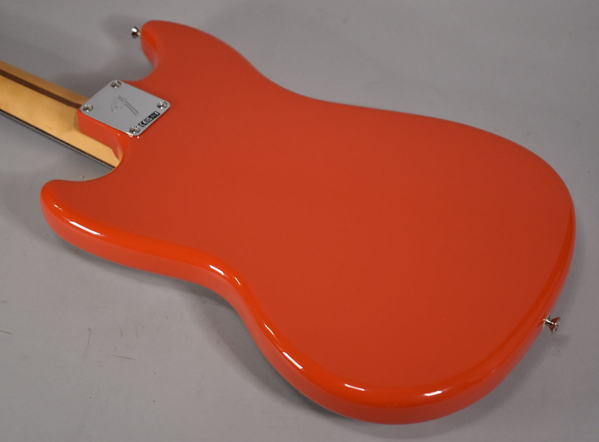 The back of a glossy Rallye Orange bass body, angled from the upper left, with a chrome neck plate and strap button visible.