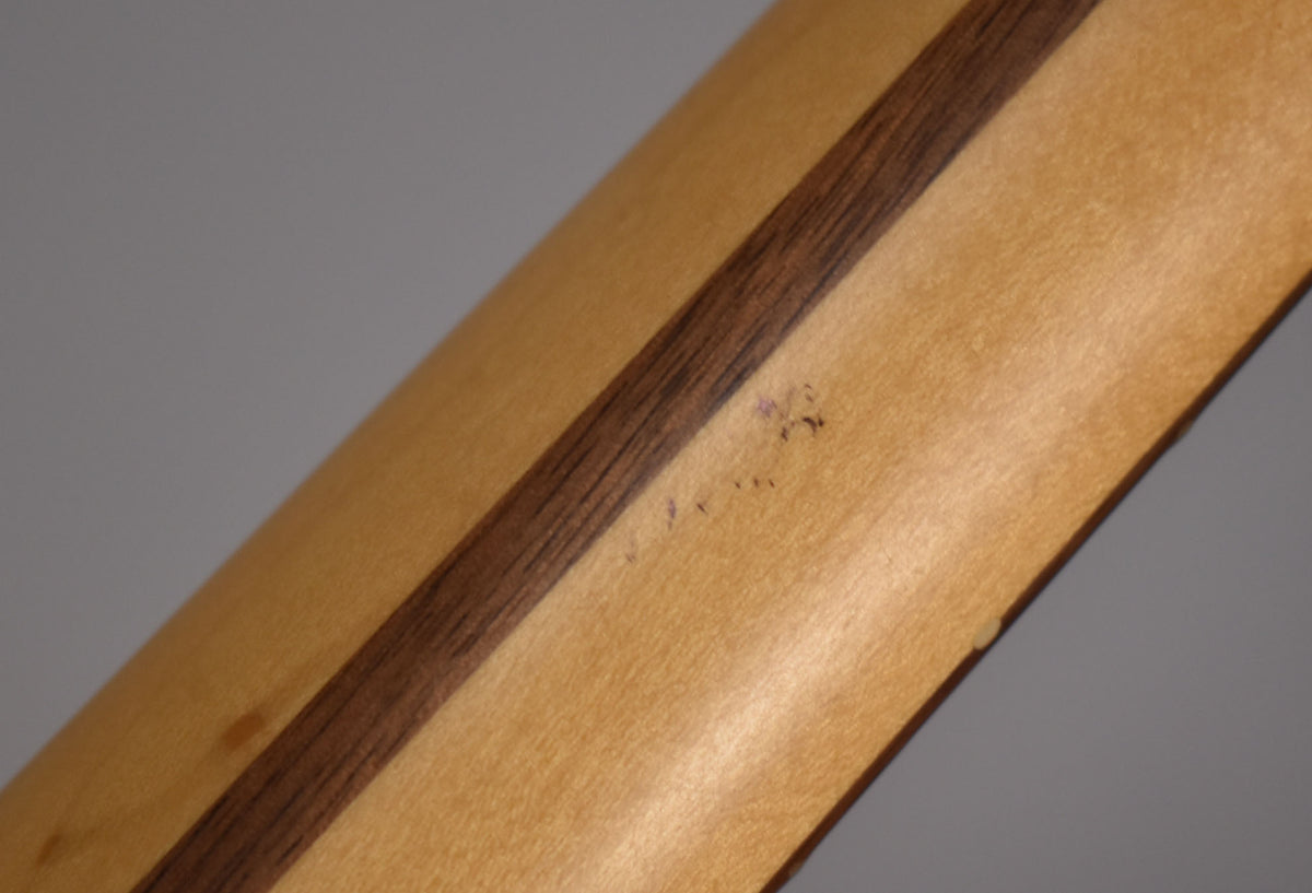 Close-up of the bass neck's back, showing a dark wood stripe down the center and several small dark scuffs on the light wood.