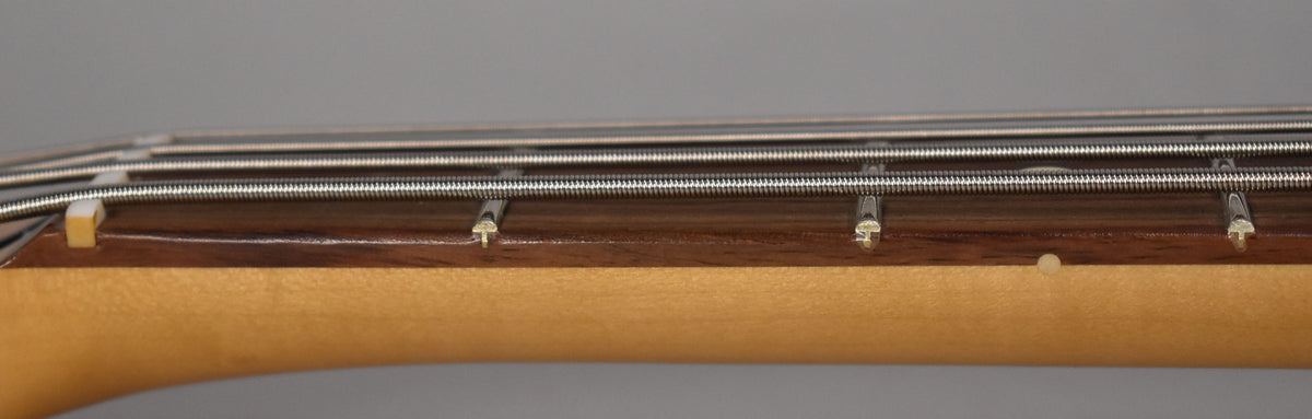 Close-up of the bass neck from the side, showing the light-colored maple neck, dark fretboard, and four strings over the frets.