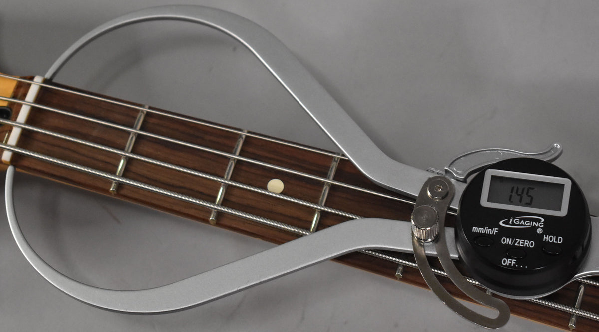 A digital caliper measures the dark wood fretboard and strings, showing "1.45" on its screen.