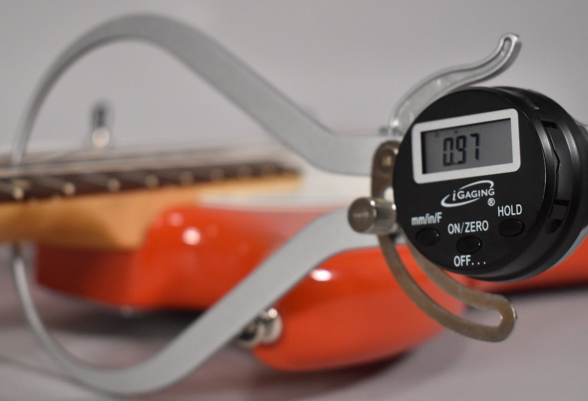 A digital caliper measures the neck relief of the orange bass, displaying "0.97" on its screen.