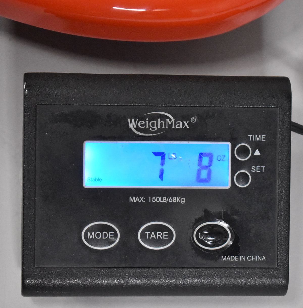 A close-up of a digital scale showing "7 LBS 8 OZ" with a small portion of the orange bass body visible at the top.