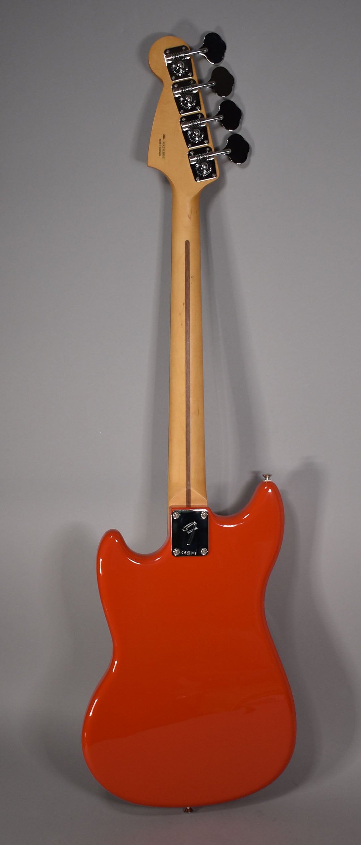 Full rear view of a glossy orange bass, showing the light wood neck, dark wood stripe, and chrome tuners.