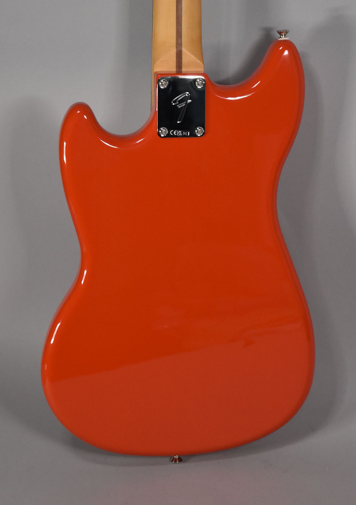 The back of a glossy Rallye Orange Mustang bass, showing the chrome neck plate and a light maple neck.