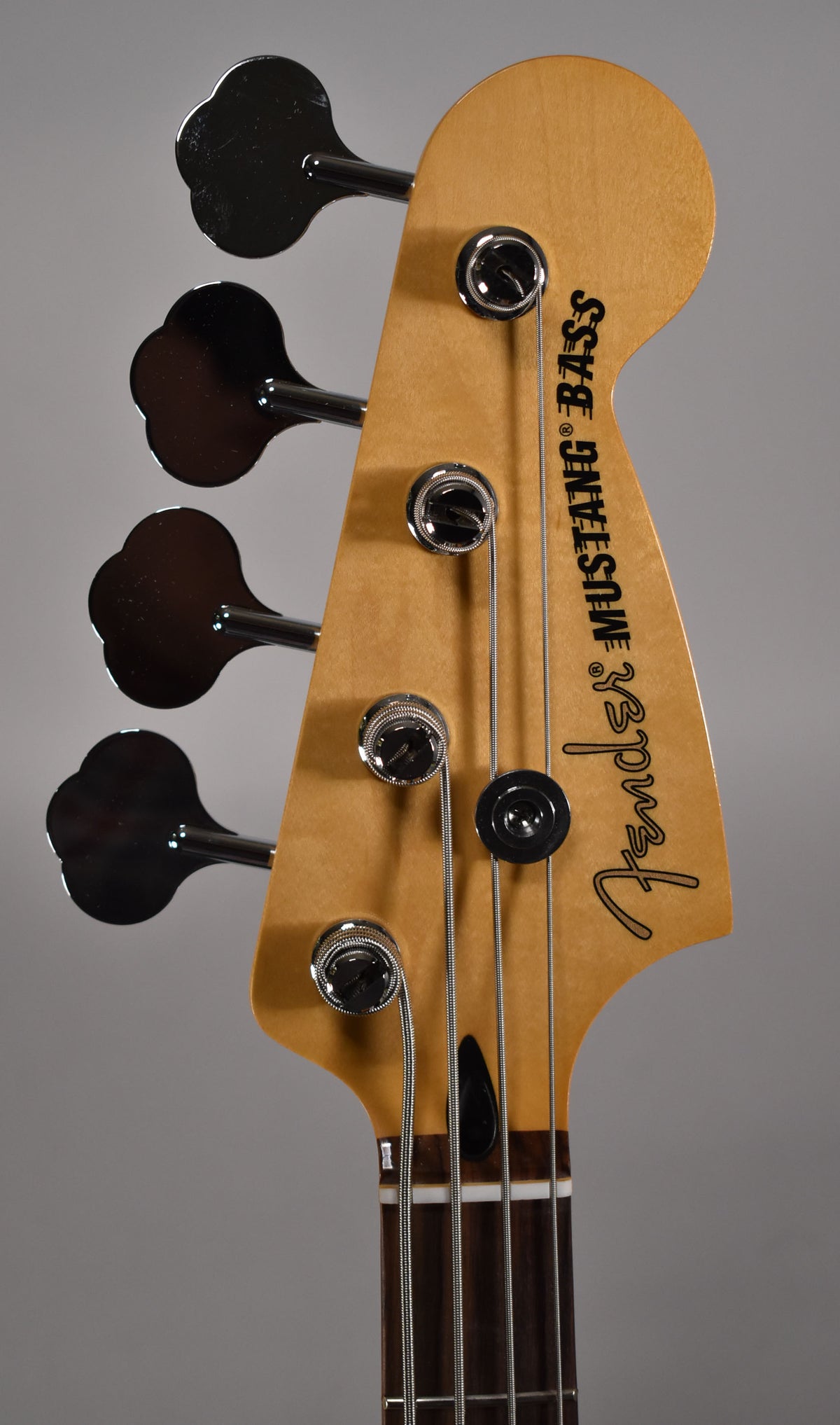 Close-up of the bass headstock, showing the light maple finish, four chrome clover-leaf tuners, and black string tree.