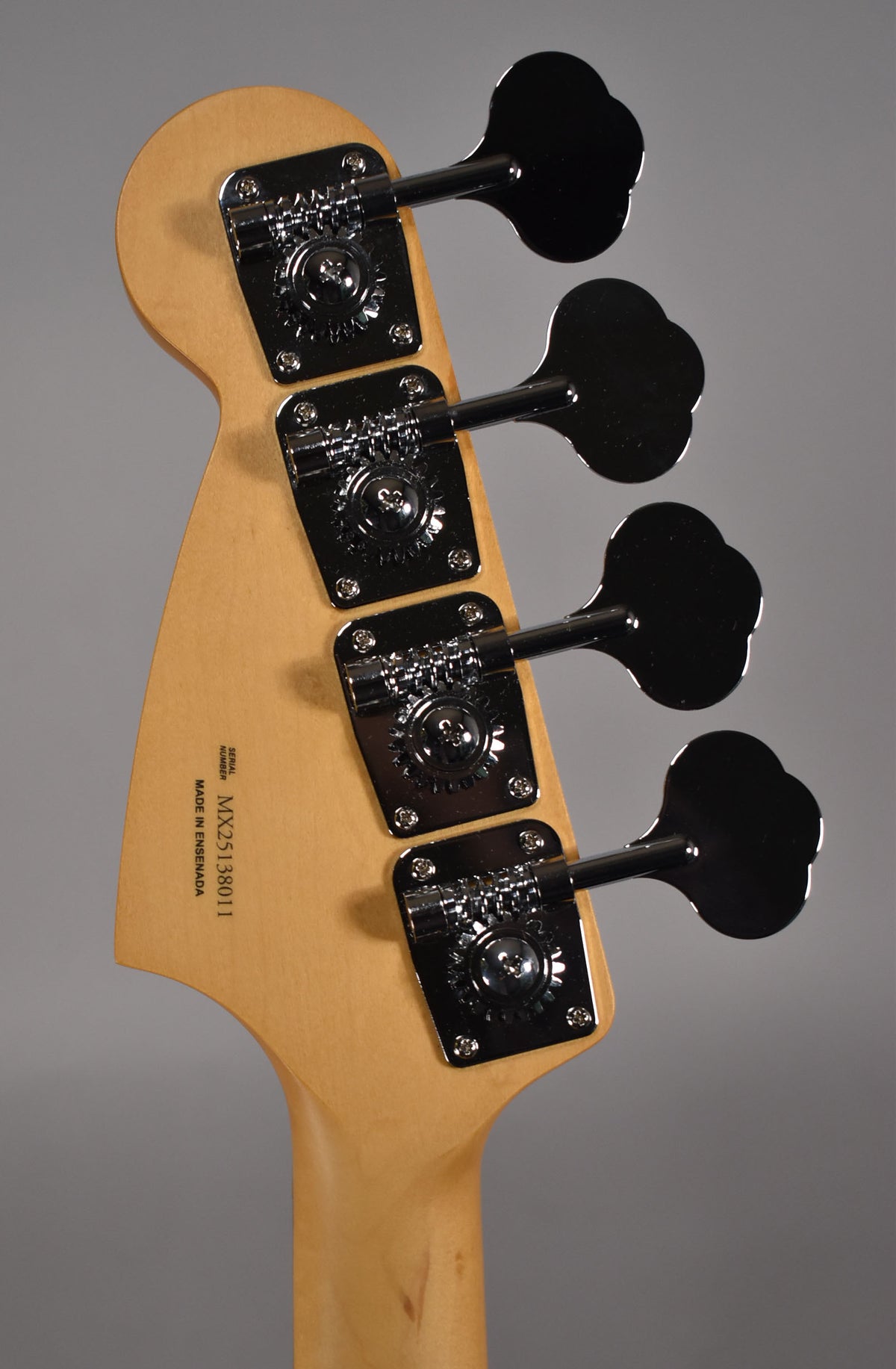 The back of the bass headstock, angled slightly left, shows four chrome clover-leaf tuners on a light wood finish.