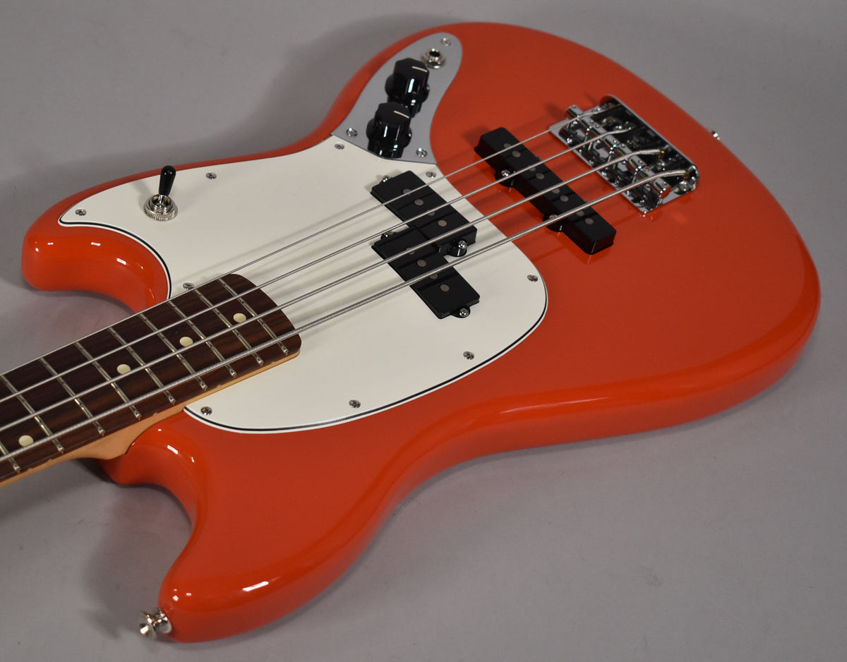 Orange bass guitar, angled from above, showing the glossy body, white pickguard, P/J pickups, and chrome bridge.
