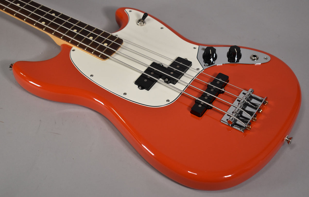 The orange bass is angled from the upper left, showing its glossy body, white pickguard, P/J pickups, and chrome bridge.