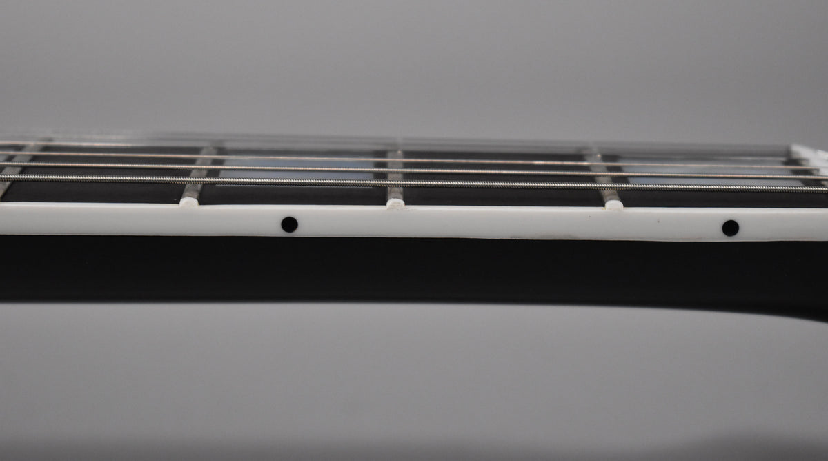 Close-up of the guitar's glossy ebony fretboard and white binding, showing the first few frets and side dot markers.