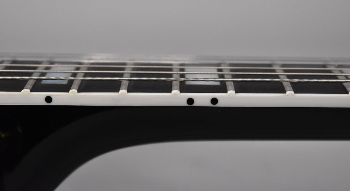 Close-up of the guitar's glossy ebony fretboard, showing white binding, fret markers, and side dots from a low angle.
