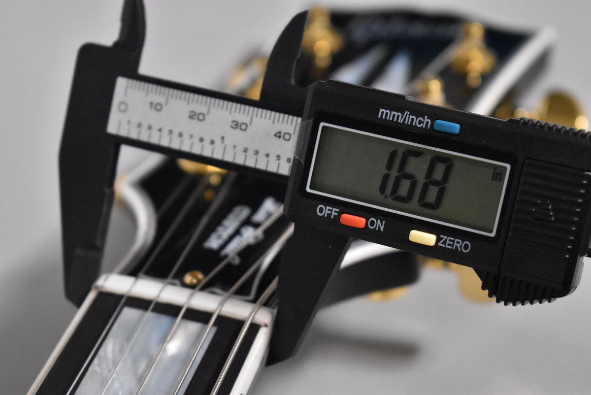 A digital caliper measures the guitar's nut width at 1.68 inches, with the black headstock and gold tuners blurred behind.