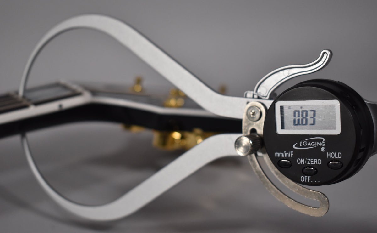 A digital caliper measures the guitar's nut width at 0.83, with the ebony fretboard and gold hardware visible in the background.