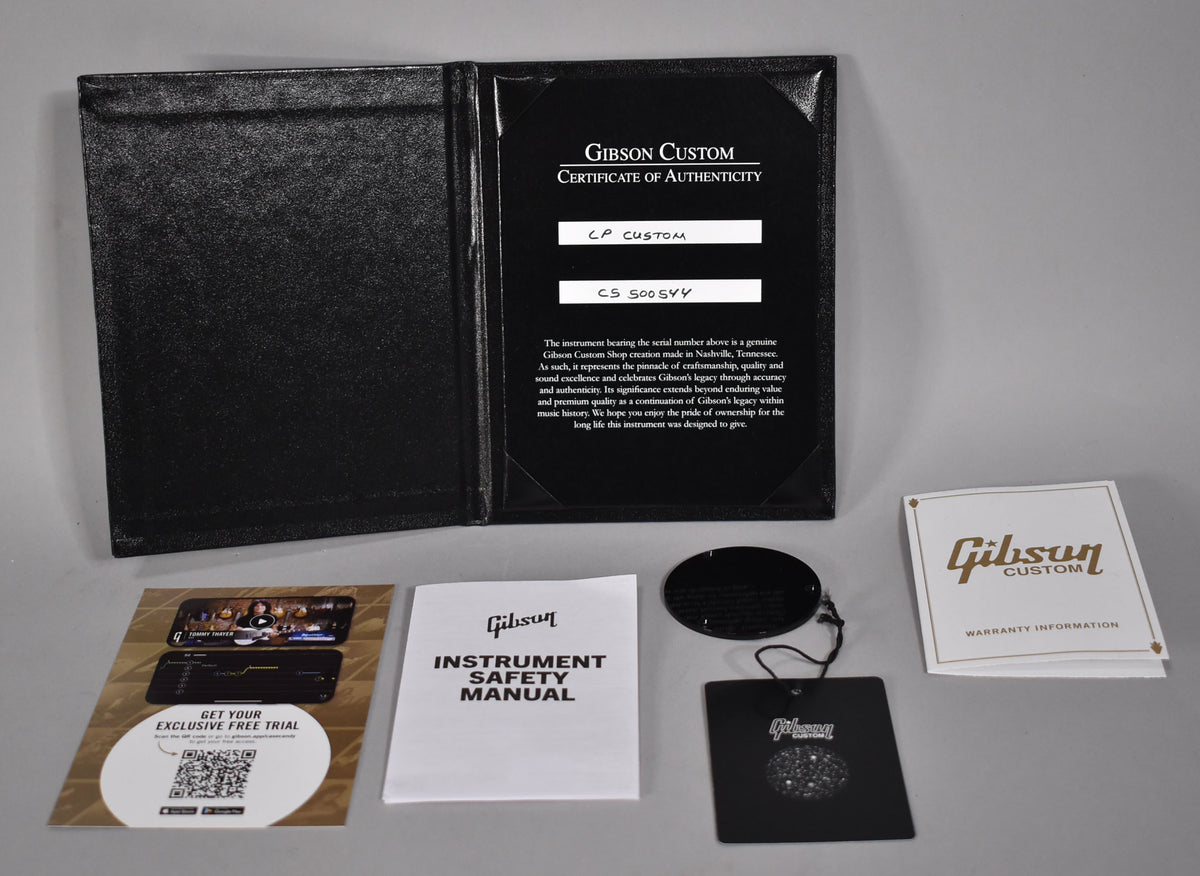 Overhead view of a black Gibson Custom Certificate of Authenticity folder, manual, warranty, and hang tags.