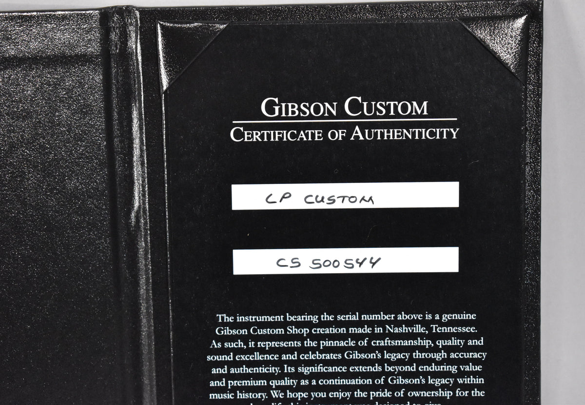 Close-up of a black "Certificate of Authenticity" for a "LP Custom" with serial number "CS 500544" in a textured black folder.