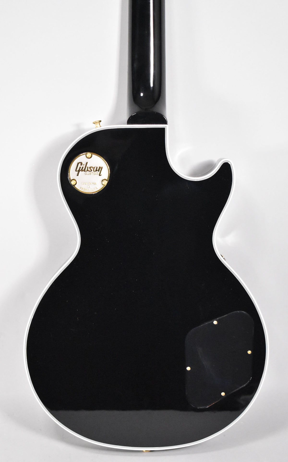 The back of a glossy black Les Paul Custom, showing the neck joint, control cavity cover, and a gold medallion.