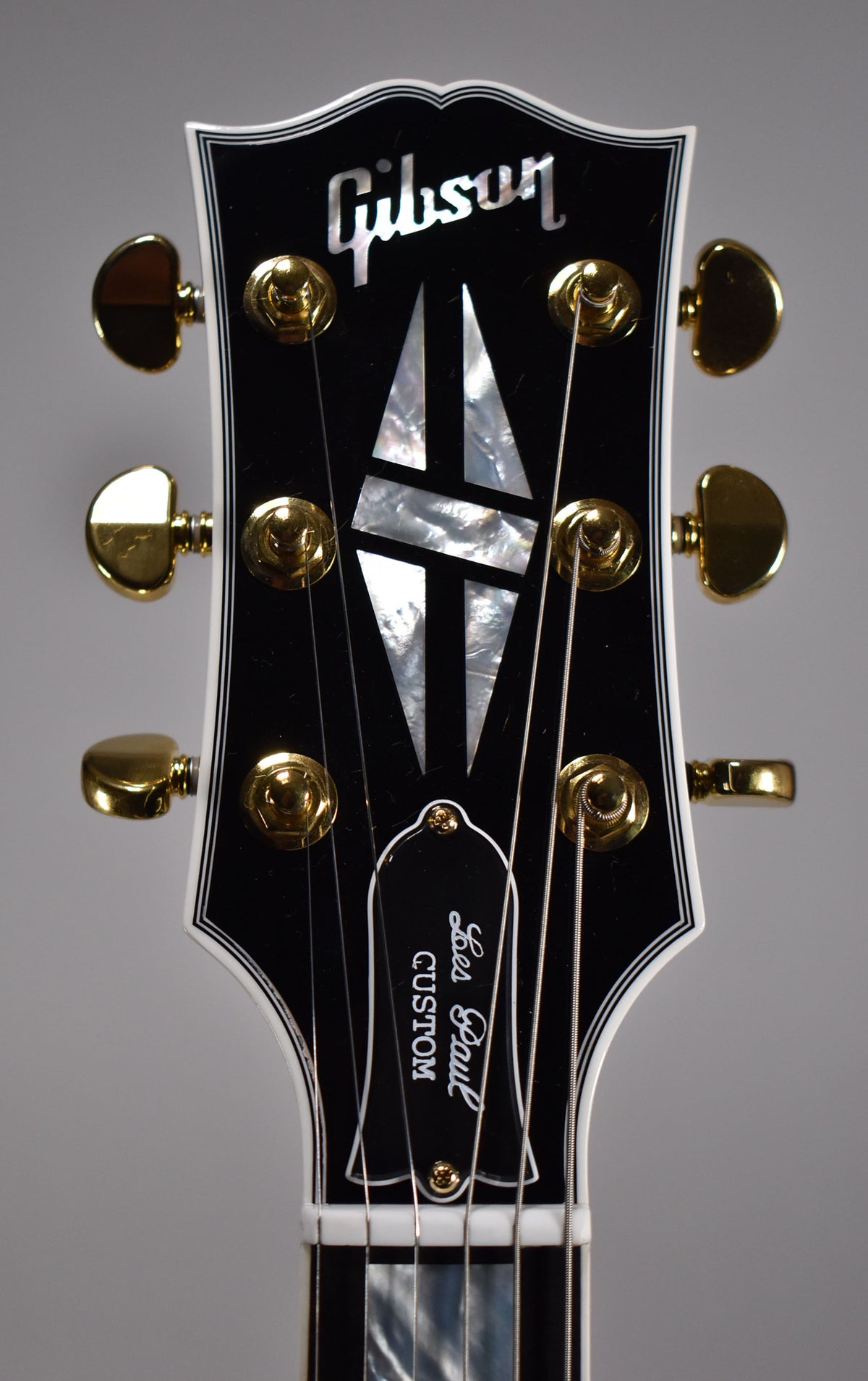 Close-up of the glossy black headstock with white binding, gold tuners, and mother-of-pearl split diamond inlay.