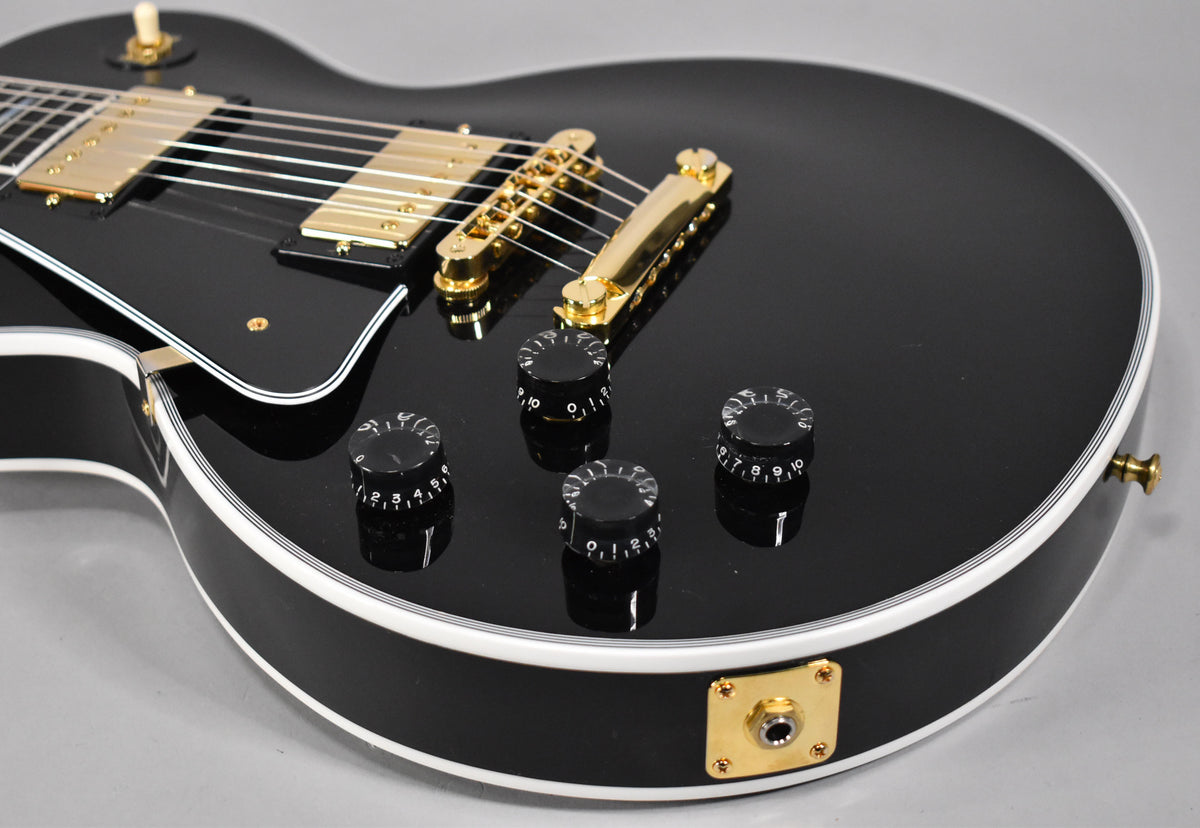 Close-up of the gloss black body, showing gold hardware, four black speed knobs, and the output jack on the lower bout.
