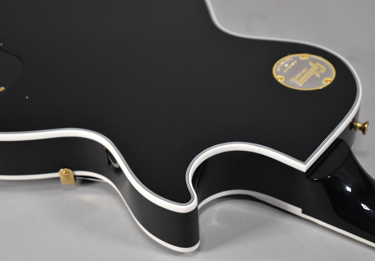 The gloss ebony body's lower bout and cutaway, with multi-ply white binding, are visible from a high angle.