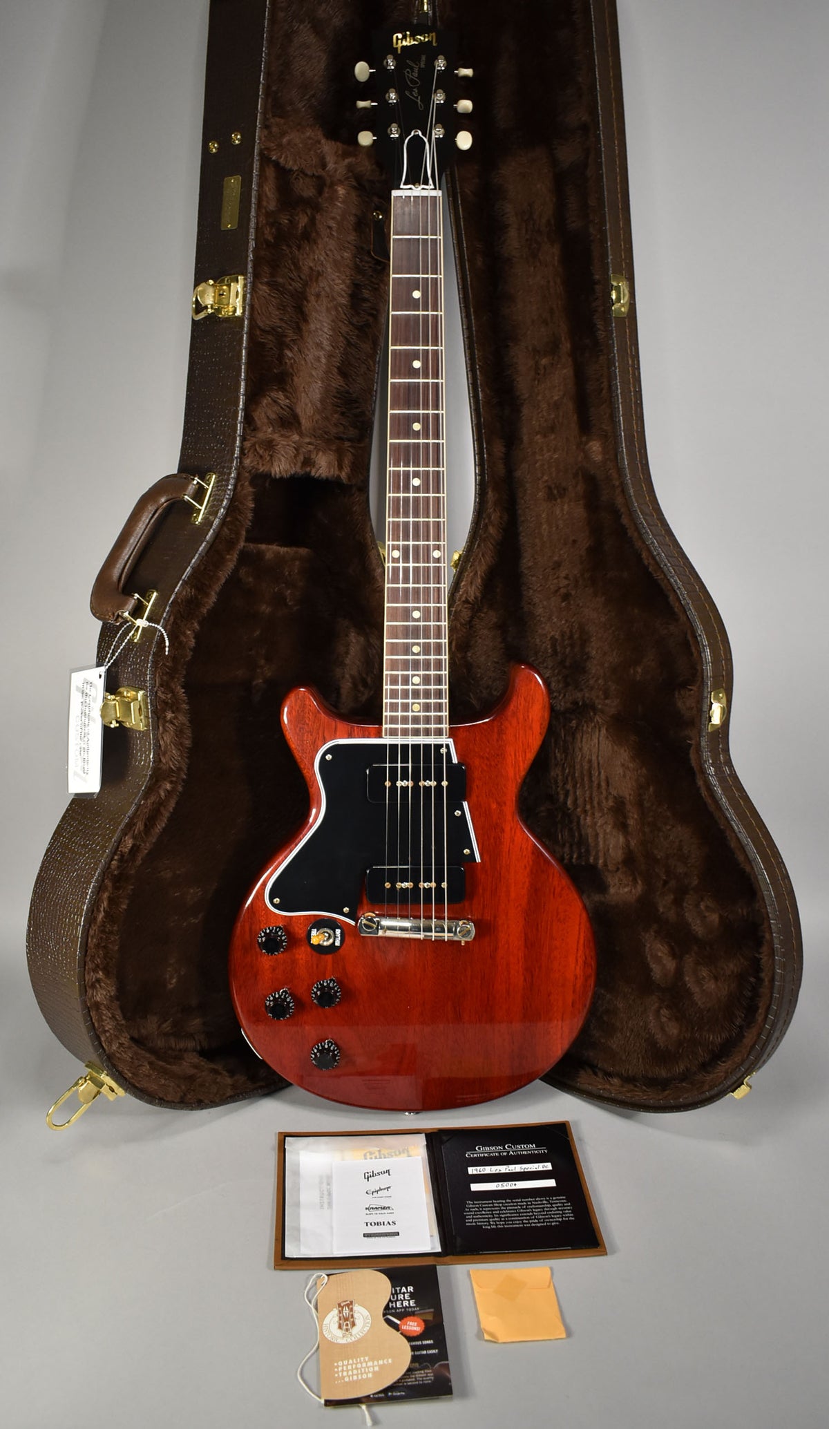 Full-length view of a faded cherry double-cut guitar with a black pickguard, P90 pickups, and four black control knobs, in its open brown case.