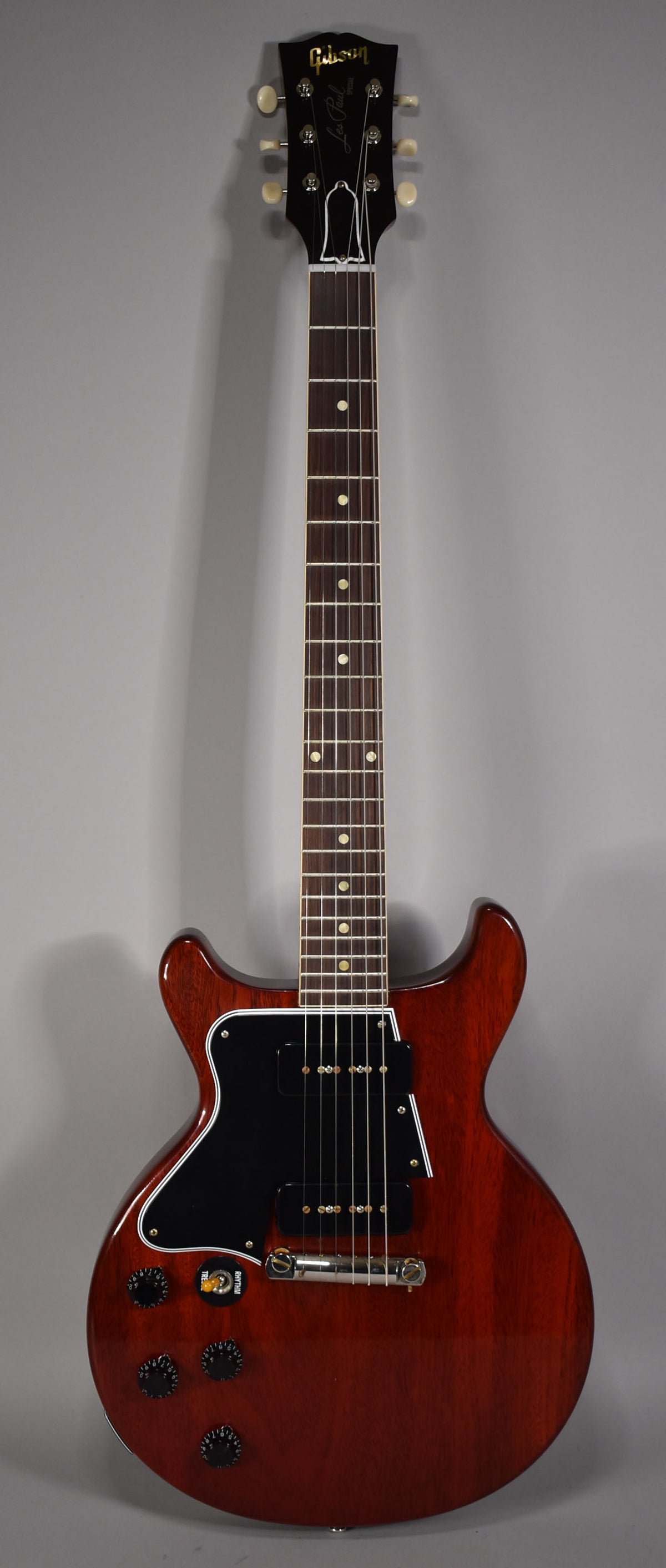 Full-length view of a faded cherry double-cut electric guitar with a black pickguard, two P90 pickups, and four black control knobs.
