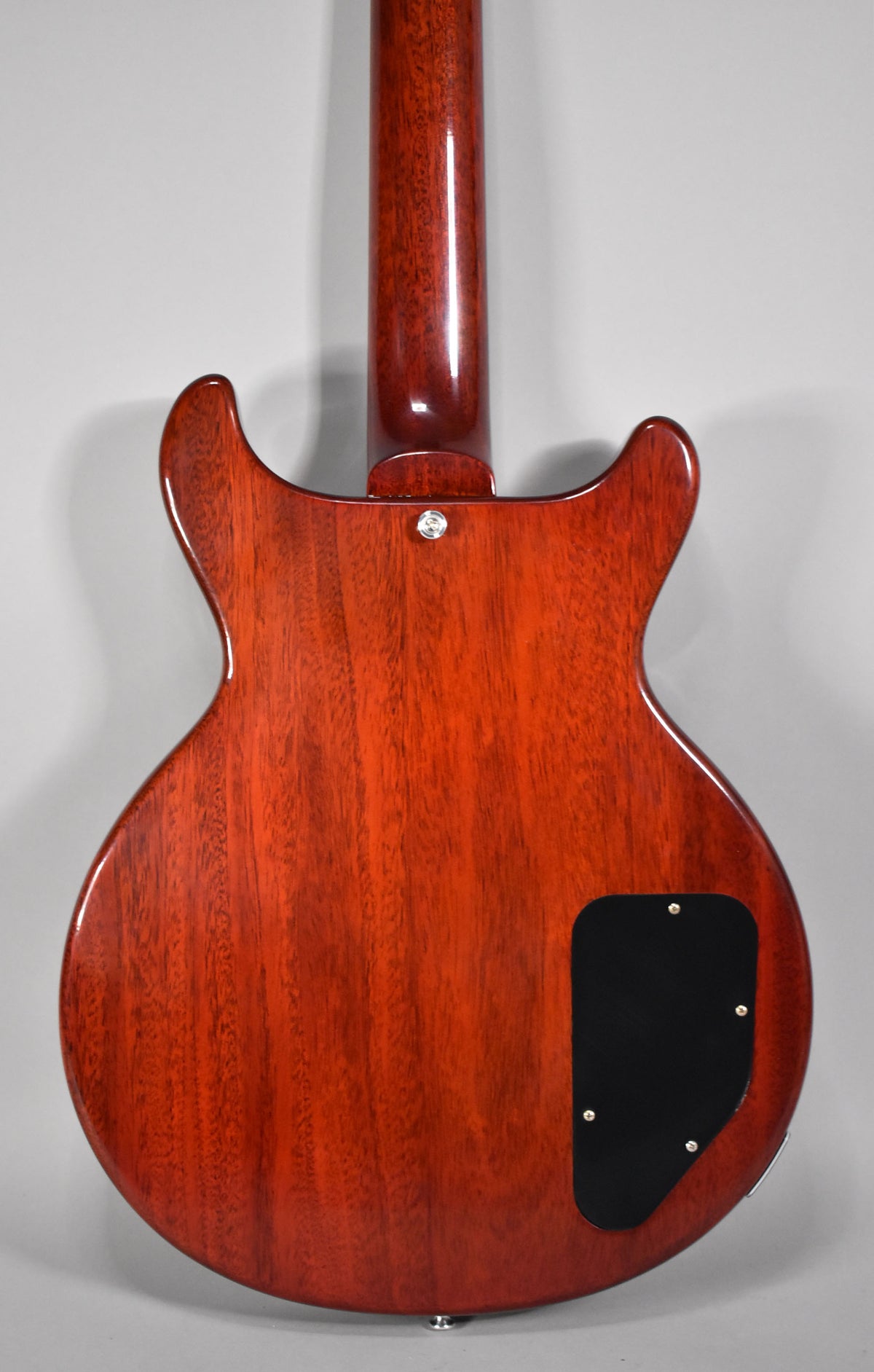 The back of a faded cherry double-cut guitar, showing the neck joint and a black control cavity cover.