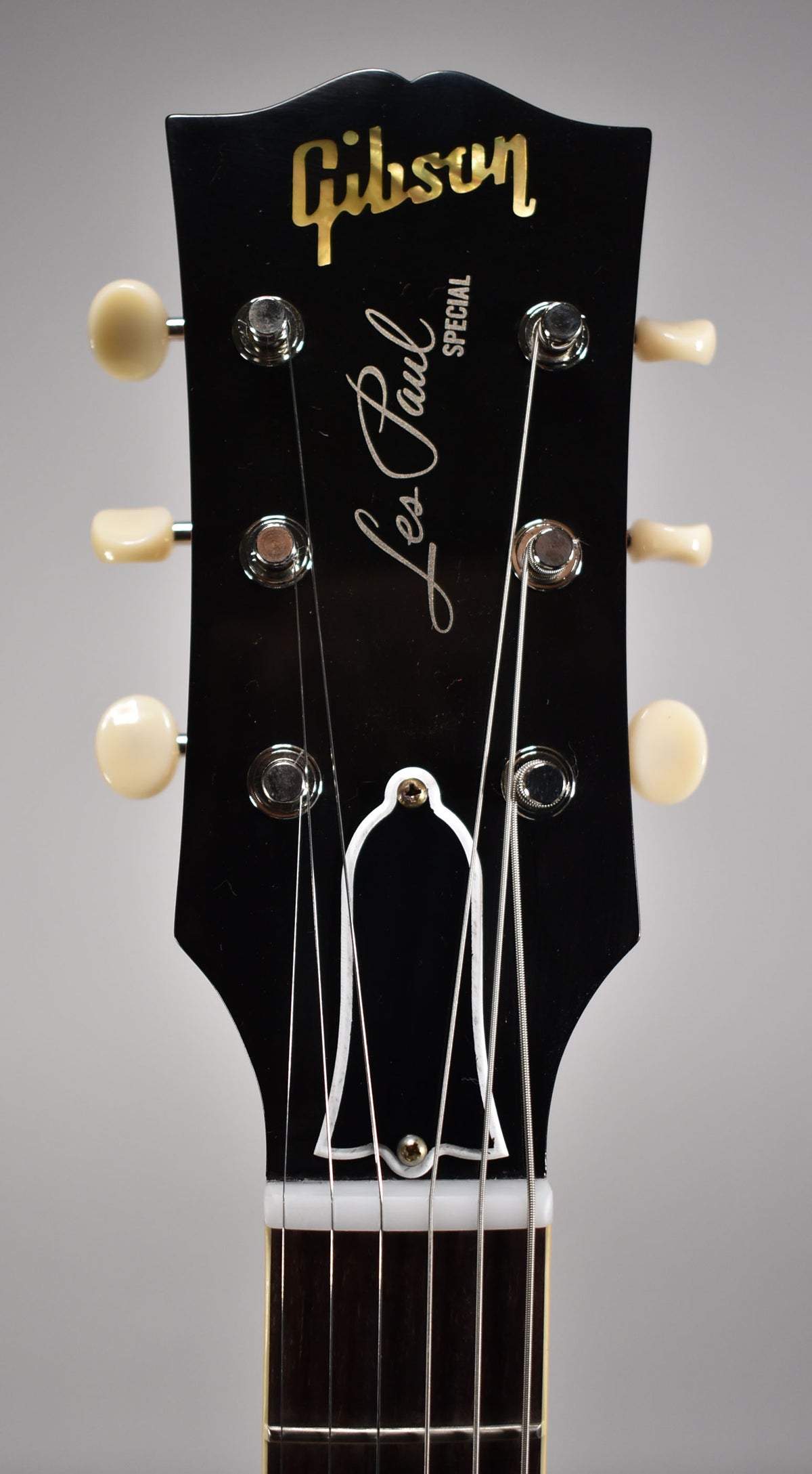 Close-up of the black headstock with cream tuners, showing the top half of the nut and strings, and the bell-shaped truss rod cover.