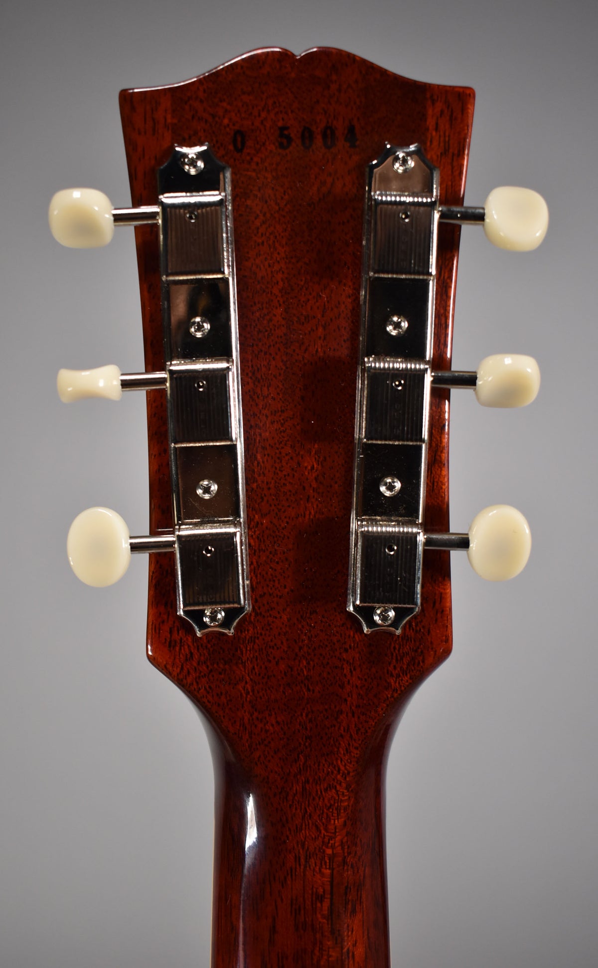Rear view of the cherry-finished headstock and neck, showing six cream-button tuners and a faint "0 5004" serial.