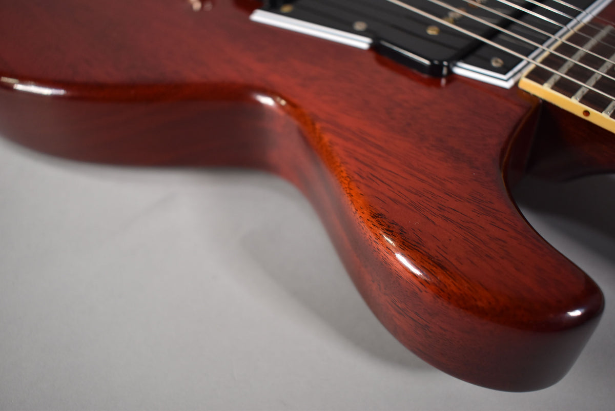 Close-up of the faded cherry guitar body's lower horn, showing wood grain, gloss finish, and a black pickup with strings.