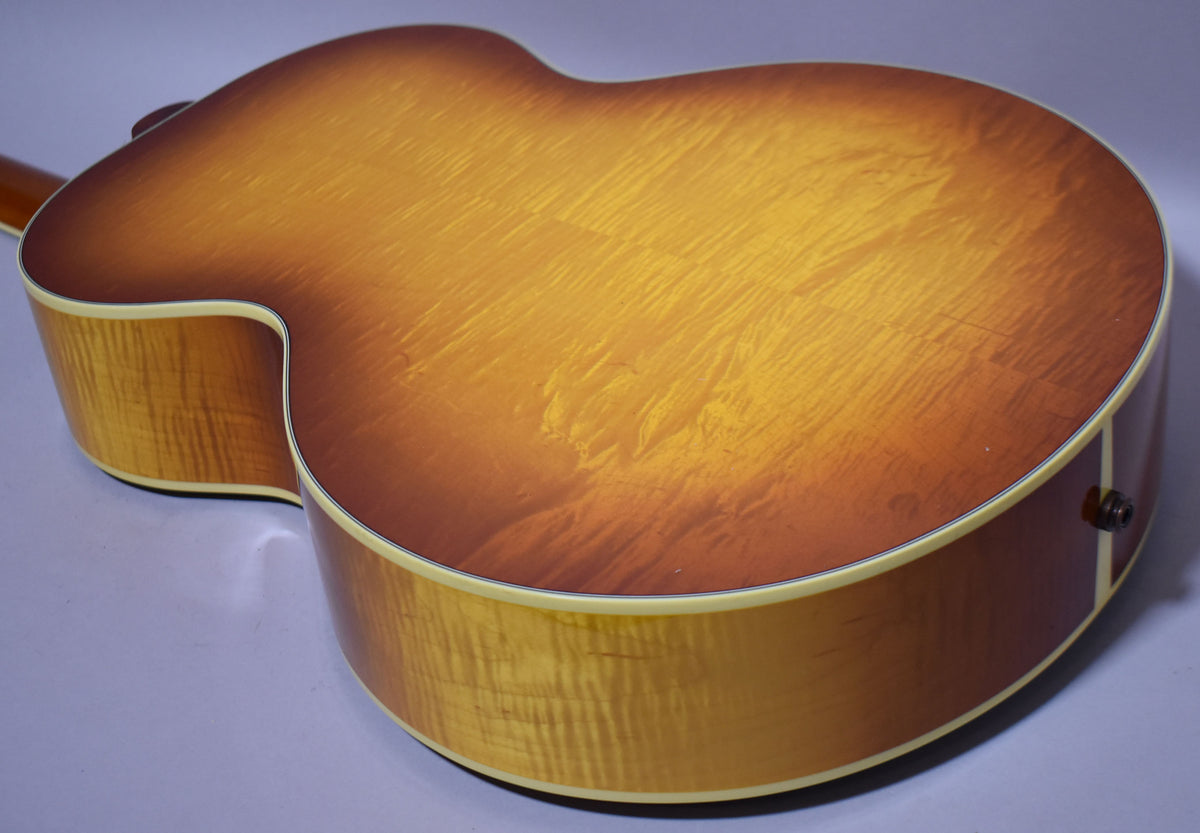The back of a cherry sunburst acoustic guitar, showing flame maple grain and a visible scratch on the lower bout.