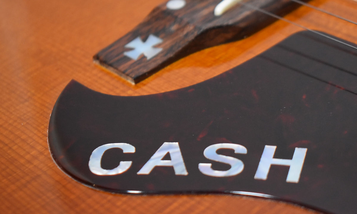 Close-up of the guitar's cherry sunburst body, showing a dark tortoiseshell pickguard with "CASH" inlaid in mother-of-pearl.