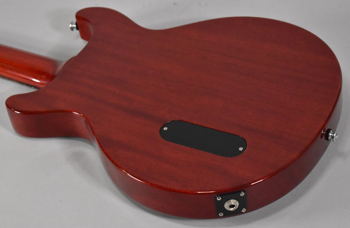 The back of a cherry red guitar, showing the control cavity cover and output jack, with visible wood grain.