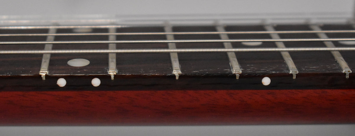Close-up of the dark fretboard and strings, showing white dot inlays on the fretboard and side, with some finish wear along the edge.