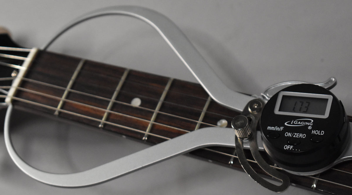 Close-up of the guitar's dark fretboard with dot inlays, strings, and a digital string action gauge displaying "1.73".