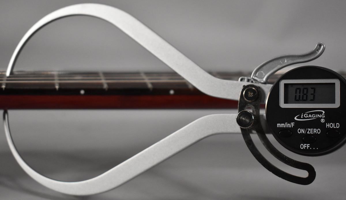 A digital fret height gauge measures 0.83mm on the guitar's dark cherry fretboard with dot inlays and silver frets.