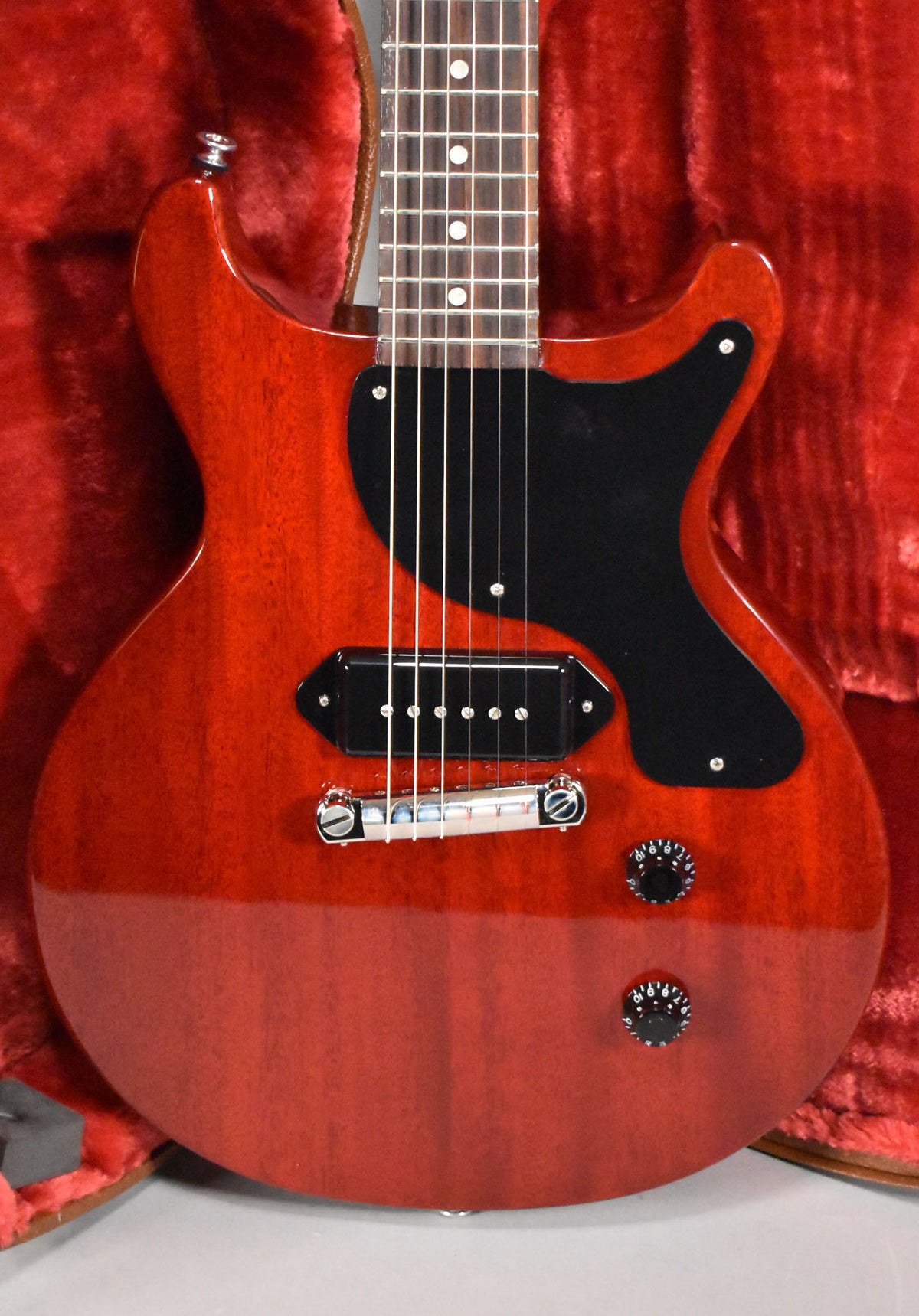 The cherry red double-cutaway body, black pickguard, single P90 pickup, and two black control knobs are framed from the waist up.