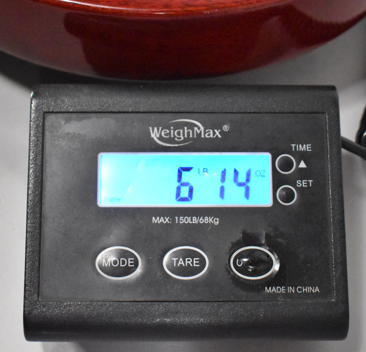 A close-up of a black digital scale displaying "6 LB 14 OZ" in blue, with the guitar's cherry finish visible at the top.