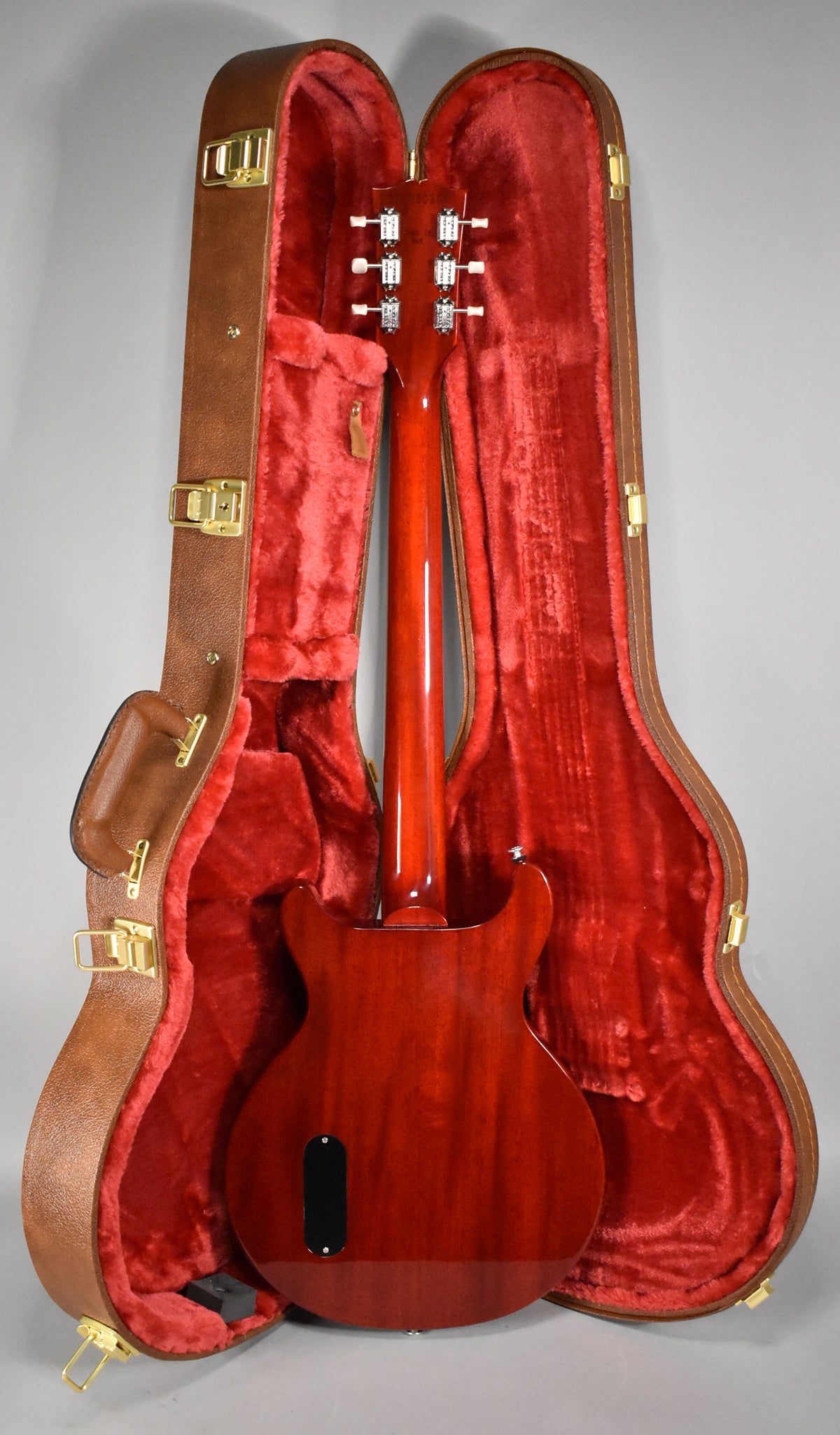 The back of a cherry-finished guitar with a black control plate, in an open brown hardshell case with red plush lining.